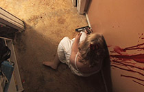 A woman shoots herself. Blood drips down the wall.