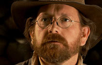 Gallery image from movie. A man in glasses with a beard looking at something.